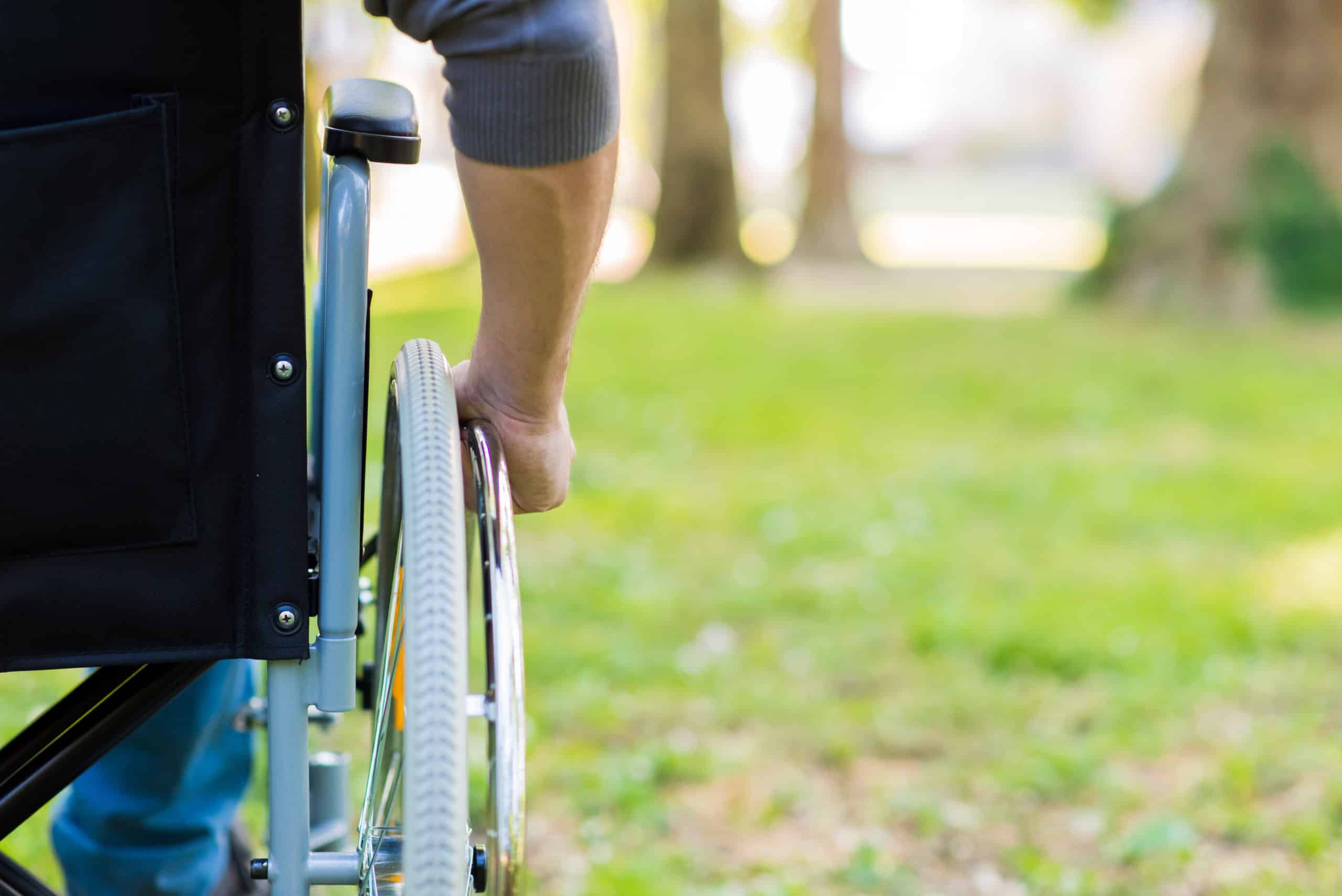 Male hand on wheel of wheelchair during walk in park