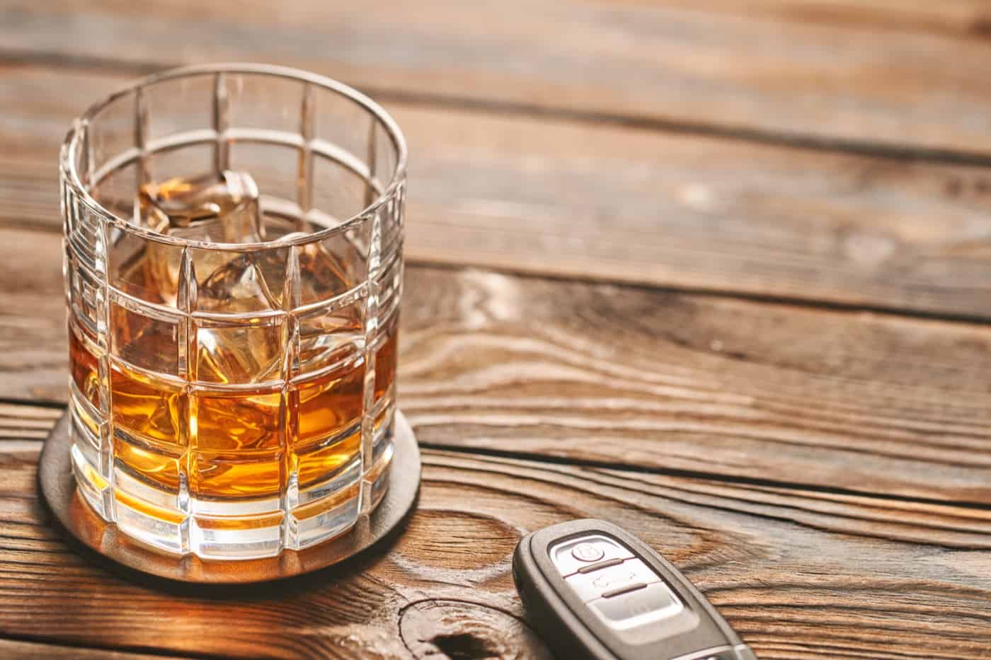 Glass of whiskey or alcohol drink with ice cubes and car key. Drink and drive concept.